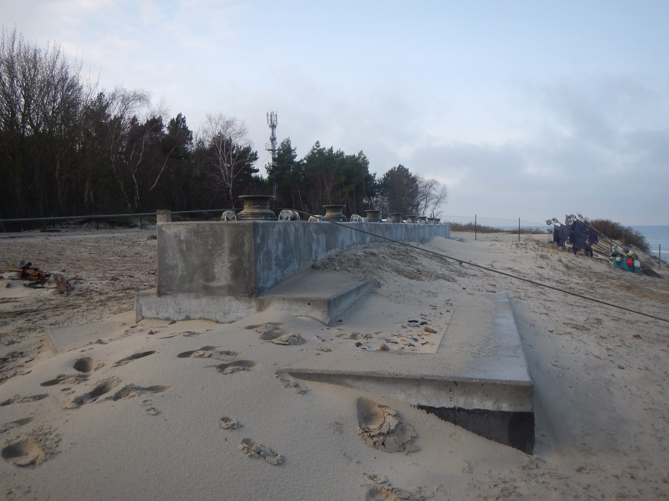 zbrojony mur na plaży z metalowymi rolkami