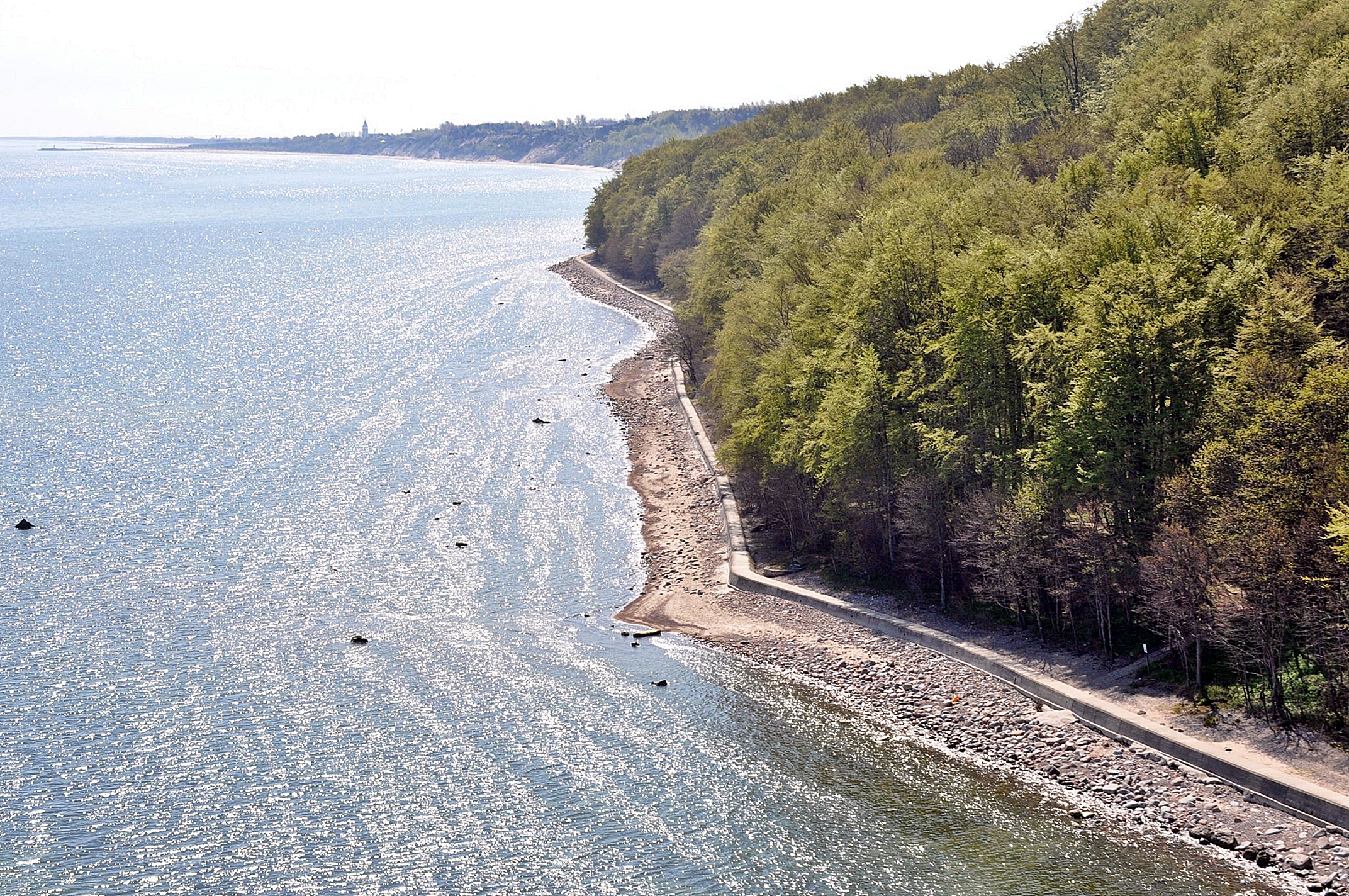 Zdjęcie z lotu ptaka ukazujące betonową opaskę brzegową u podnóża porośniętego lasem klifu.