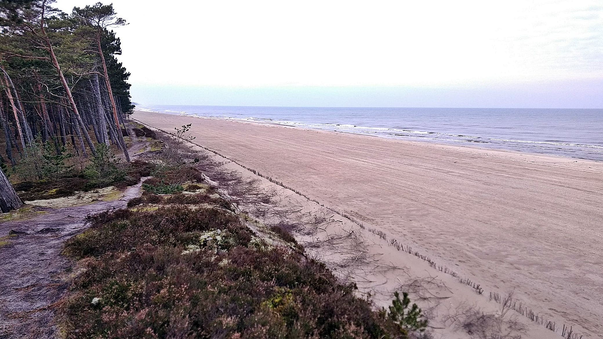 Zdjęcie szerokiej, sztucznie utworzonej w wyniku refulacji, plaży, pod którą znalazło się umocnienie w postaci opaski gabionowej.