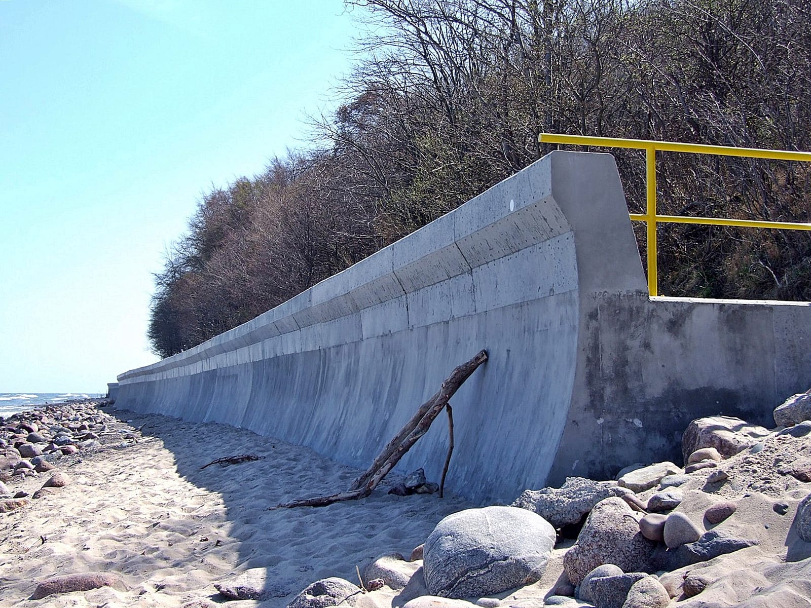 Zdjęcie betonowej opaski brzegowej z odbijaczem fal, zrobione z poziomu plaży.