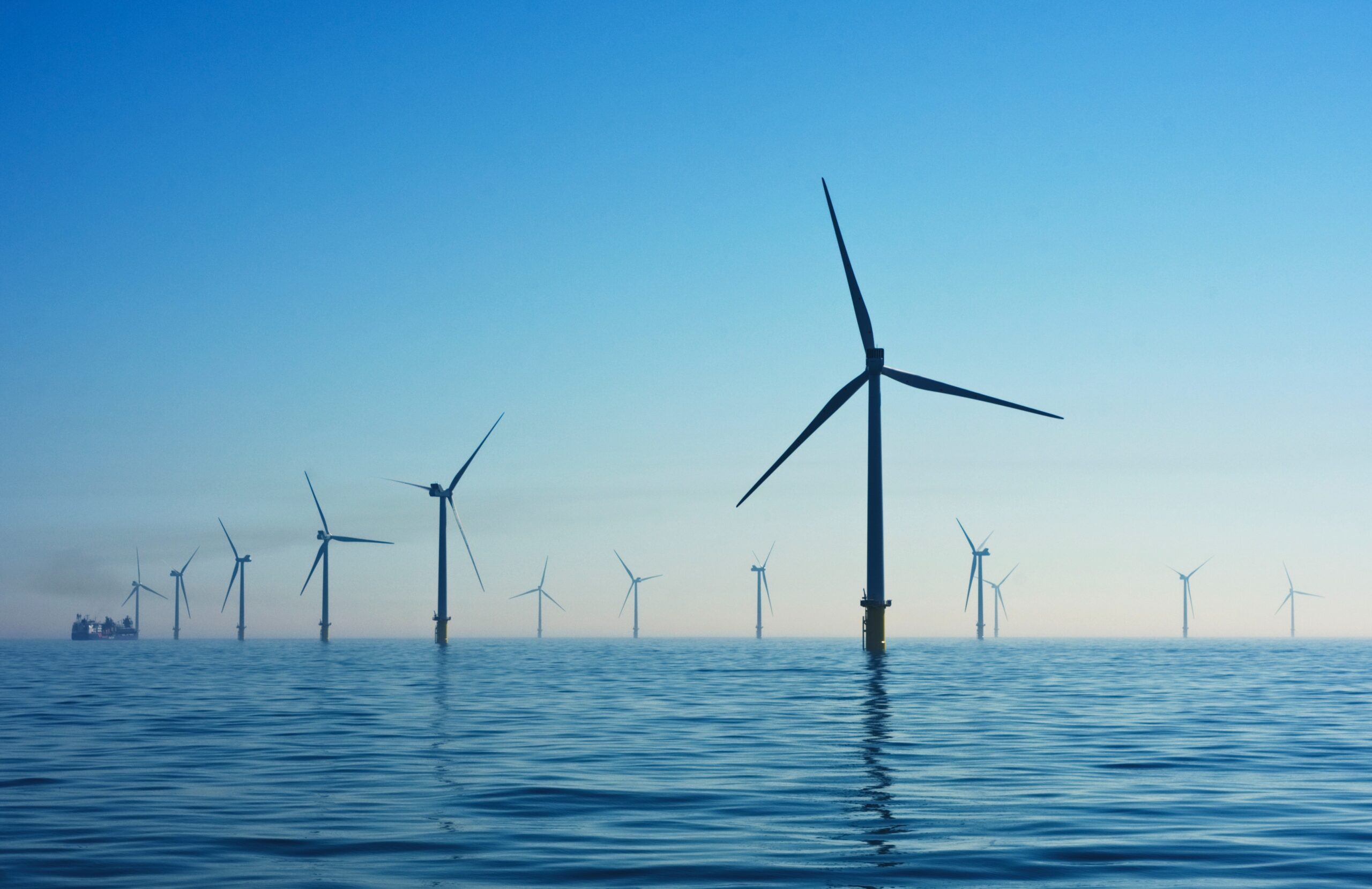 Calm sea, no waves, clear sky. A wind turbine is visible in the foreground, other wind turbines are visible in the distance 